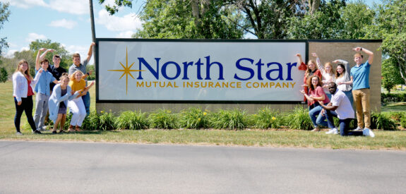 People smile and pose beside a North Star Mutual Insurance Company sign outdoors on a bright, sunny day.