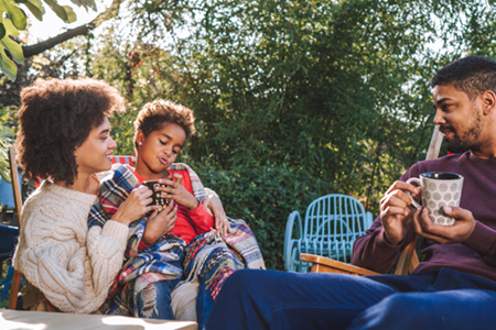 A family relaxes outside, wrapped in blankets and enjoying hot drinks together.