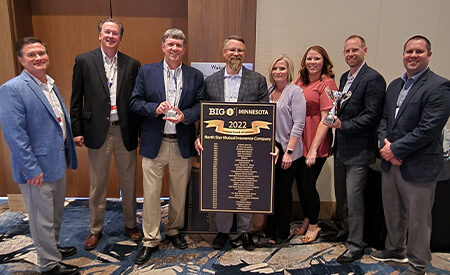 Eight people indoors, holding trophies and a large sign reading "2022 Big I Minnesota award.